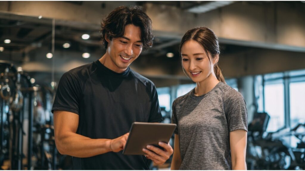 ジムでトレーナーと女性がタブレットを見ながらトレーニング内容を確認している様子